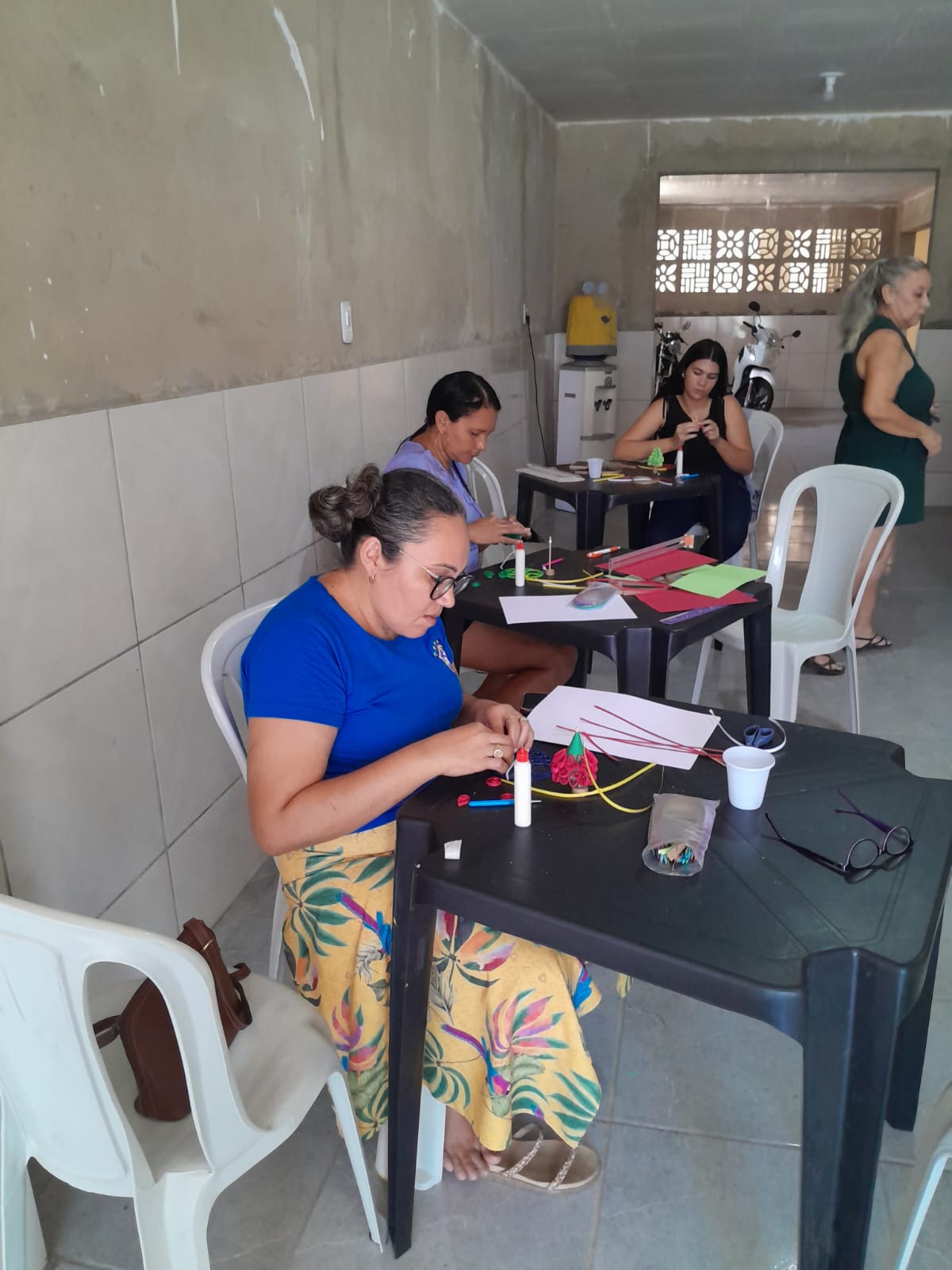 Mulheres sentadas em mesas de plástico enrolando papel colorido na oficina de quilling da Fundação.